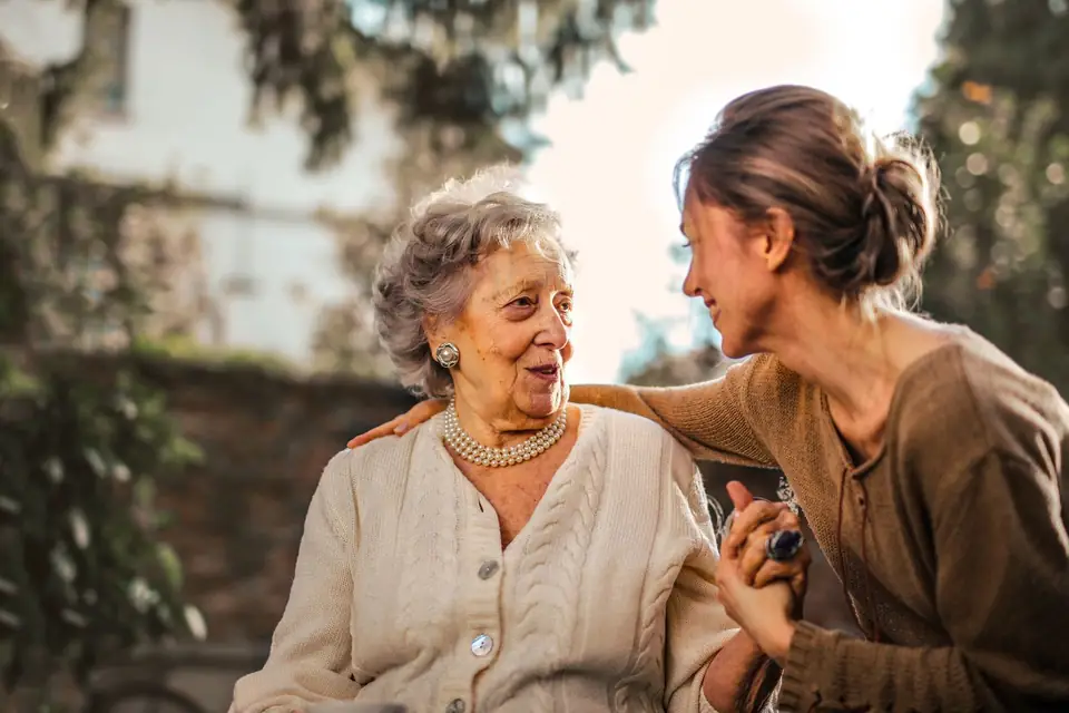 An adult daughter embraces her mother in a garden.