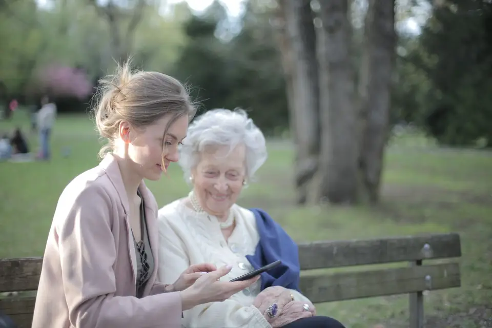 An adult daughter shows her mother a tablet while they sit together outdoors.